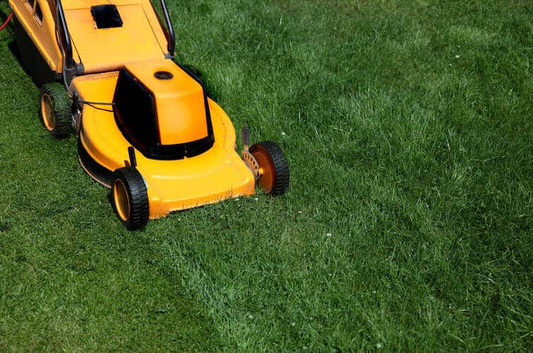 a yellow lawn mower sitting on top of a lush green field.