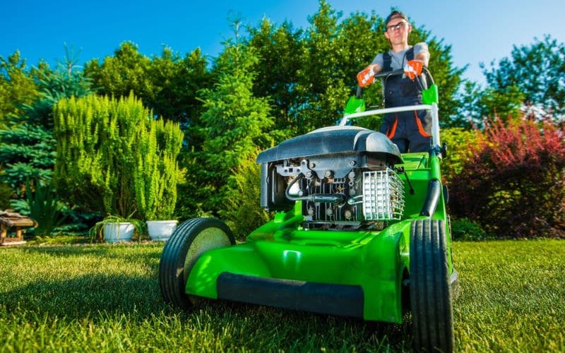 a man mowing a lawn with a green lawn mower.